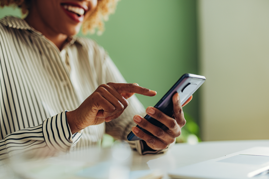 Image of a woman in a striped blouse typing and smiling on phone.