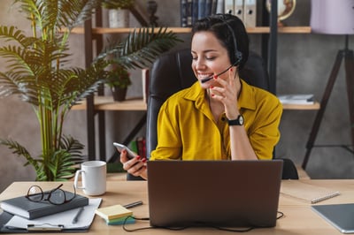 Image of a woman smiling at her laptop and looking at her phone.